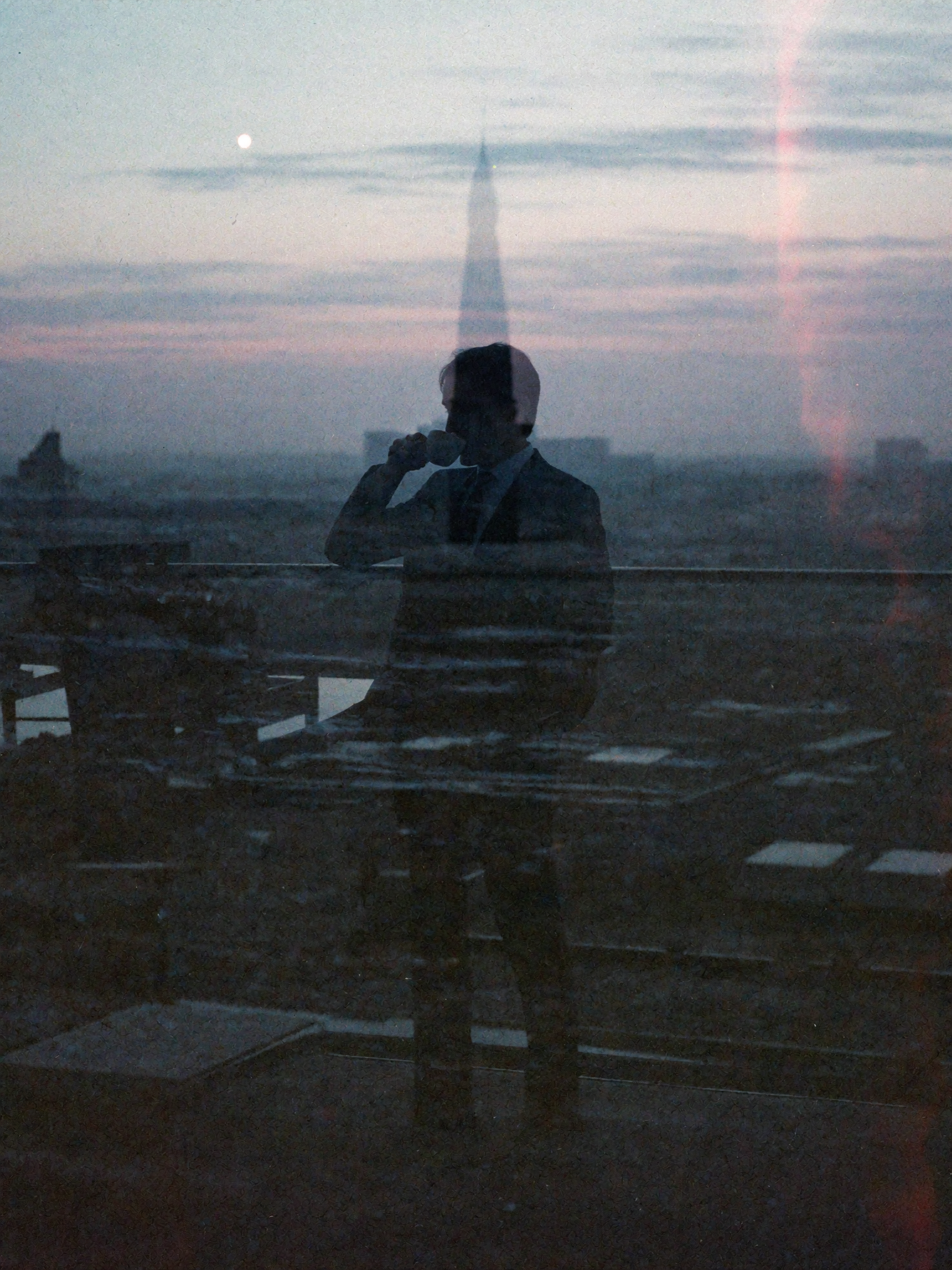 Man on a rooftop drinking coffee with a cityscape reflection
